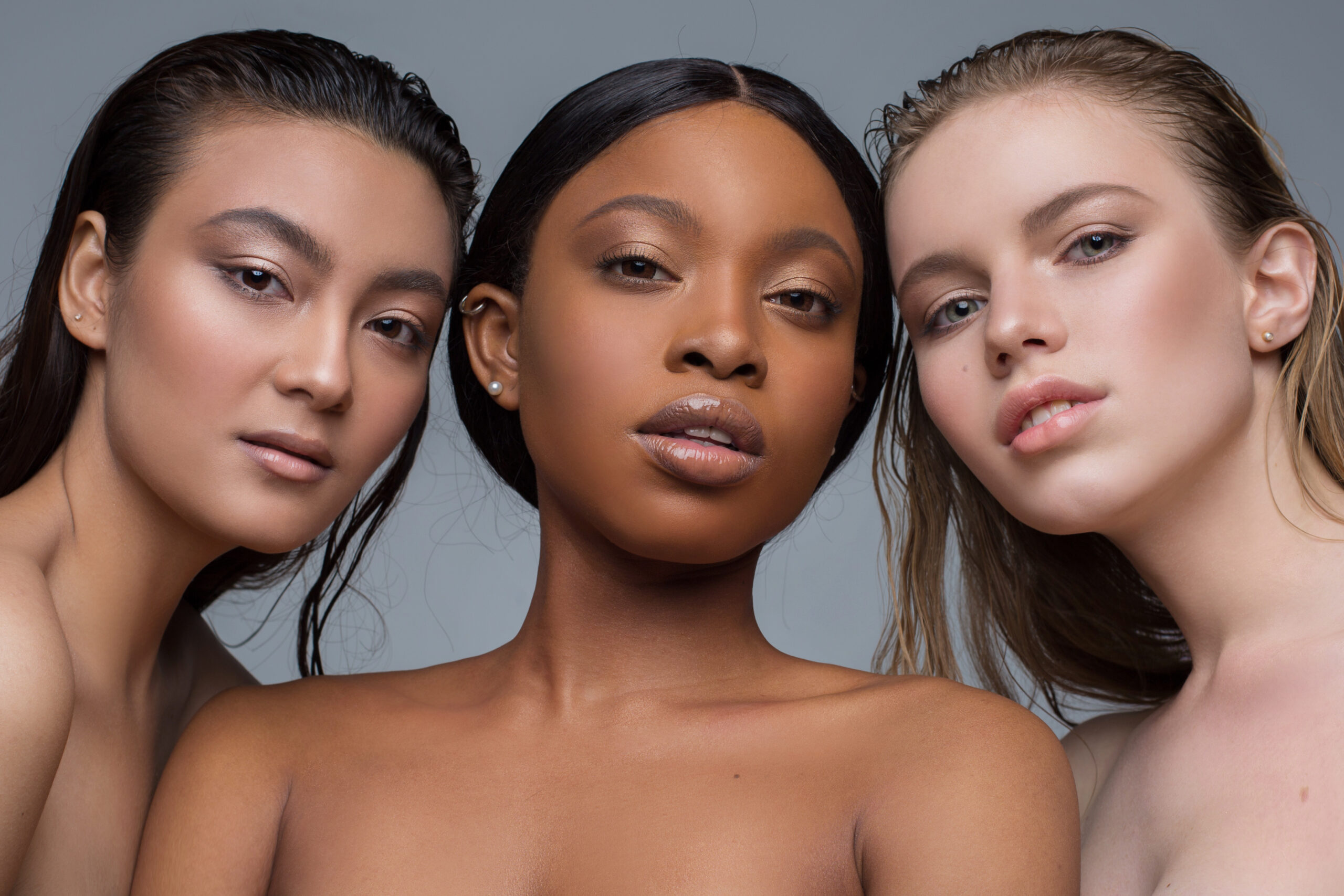 Beauty portrait of three mixed races women with natural make up and healthy skin. On gray background. Portrait caucasian and african american and asian girls different skintone